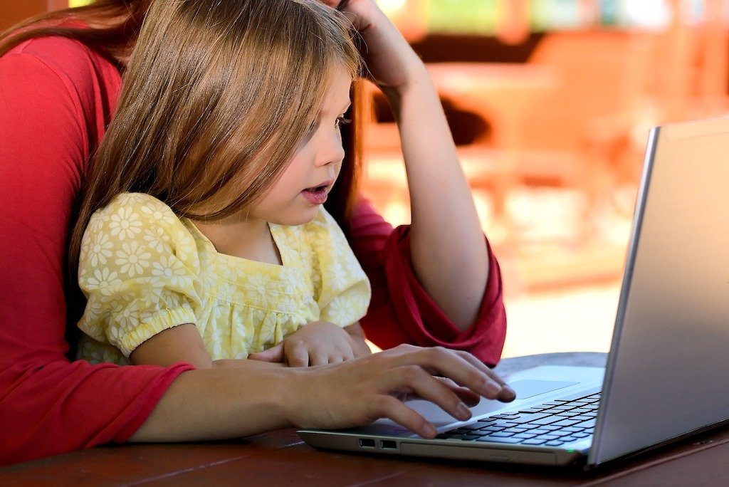 A mother uses her laptop with her daughter on her lap