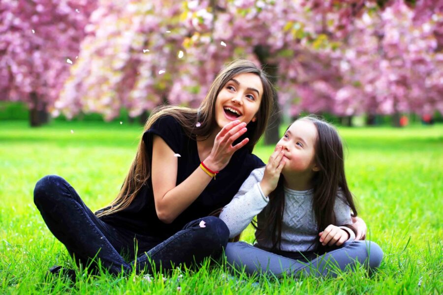 A young woman watches falling blossoms with a little girl at the park