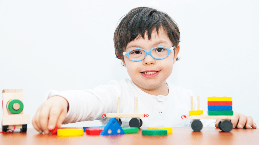 A boy wearing glasses plays with a toy train