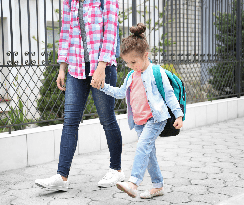 A kid watches her feet while walking to school with her mom