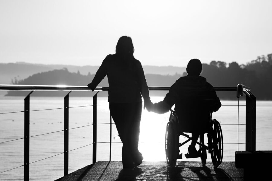 Woman and boy in wheelchair holding hands by the sea
