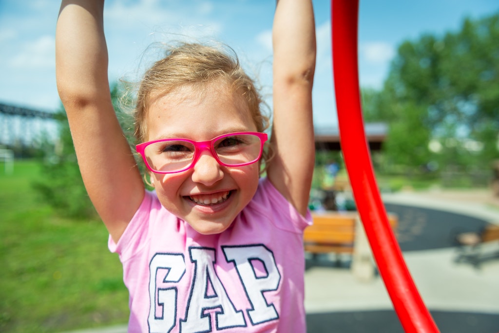 a girl with glasses hanging on monkey bars