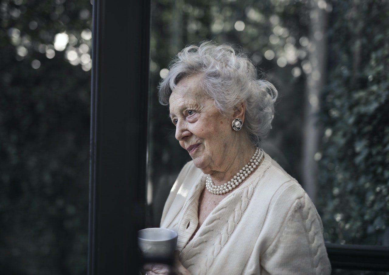 An older woman gazing out while holding a cup