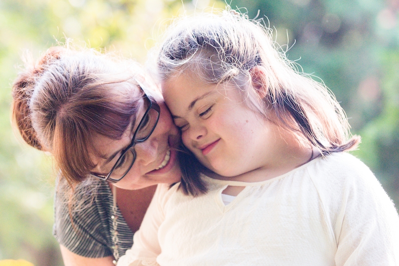 A mother embraces her autistic daughter from behind