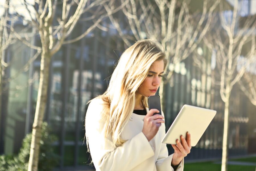 A woman reading a tablet with a phone in the other hand