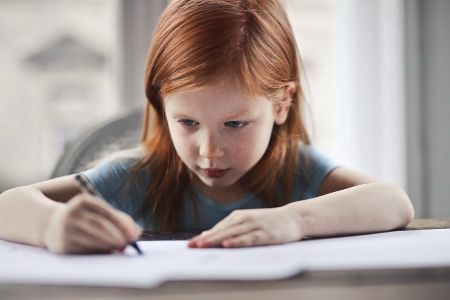 A red-headed little girl writes on paper