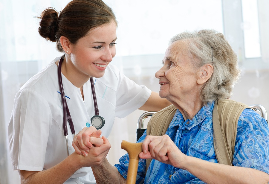 An elderly woman talks to her caregiver while holding her hand