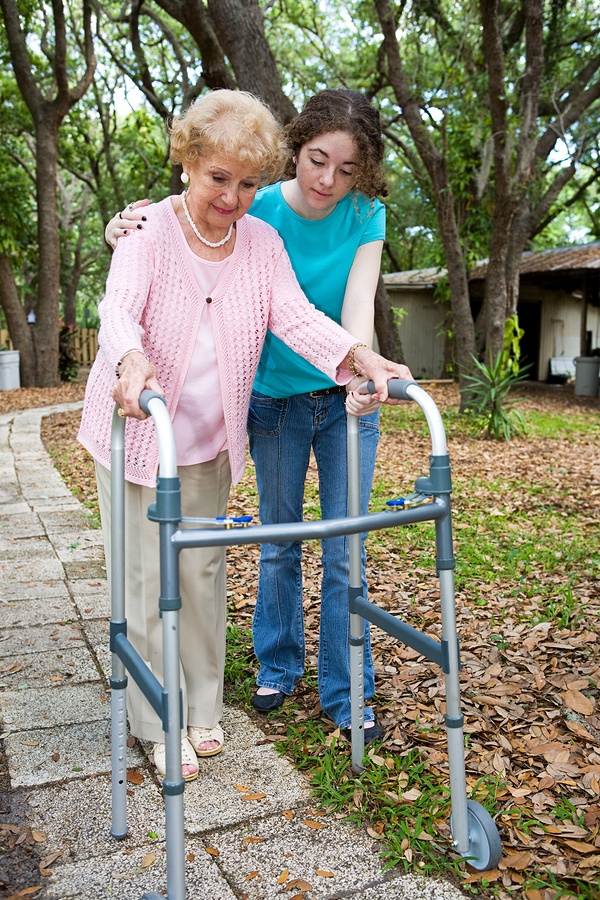 A caregiver helps a woman walk down her sidewalk