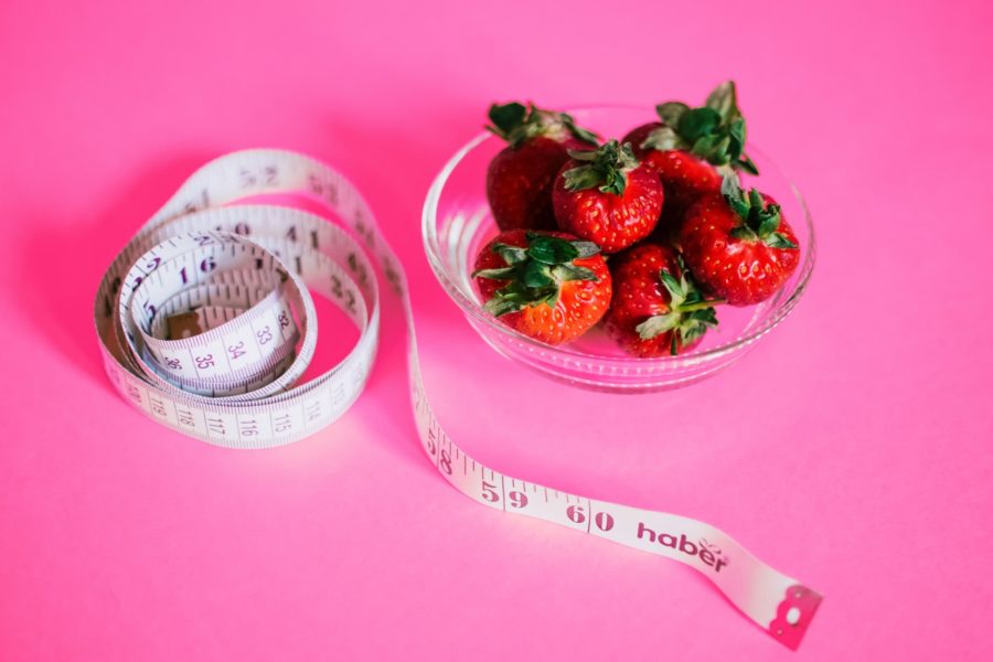 A bowl of strawberries next to a measuring tape