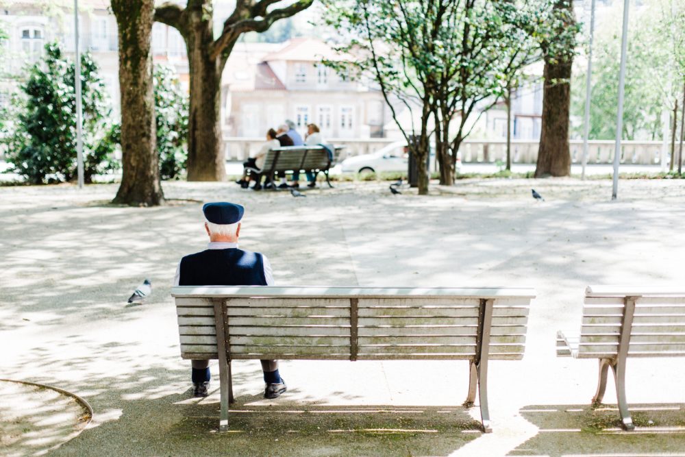 A senior man sits on a park bench alone