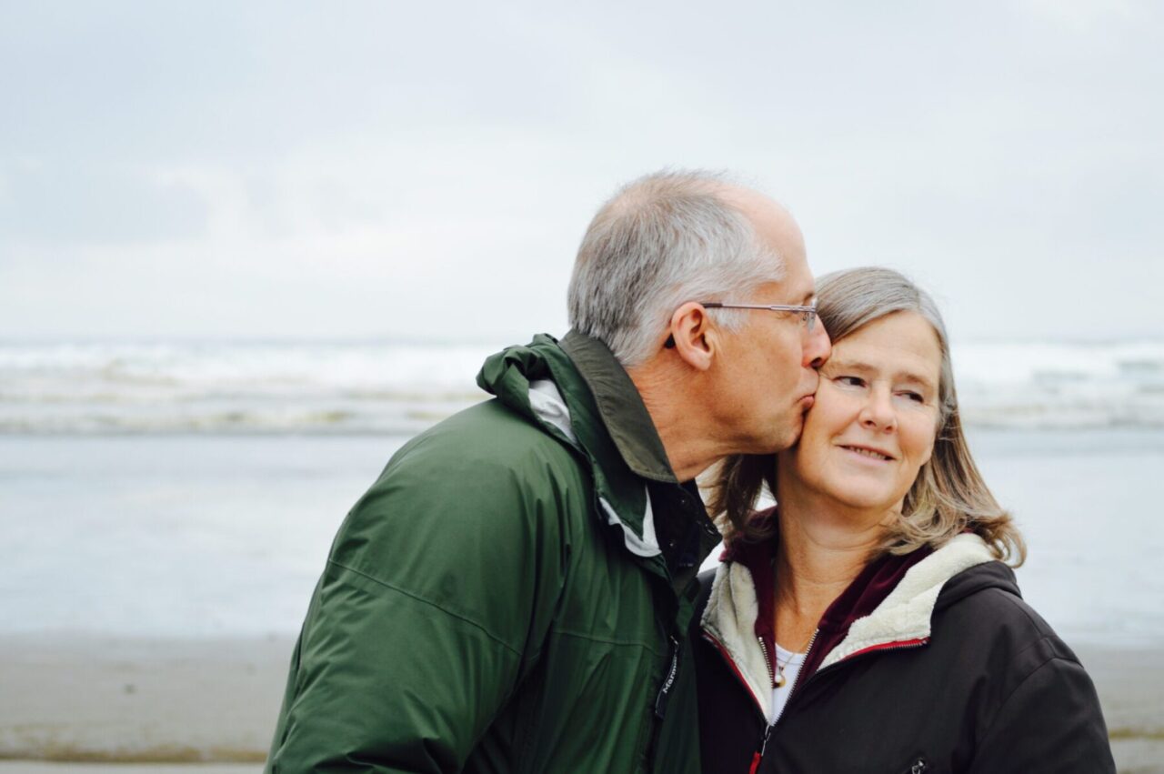 A man gives his wife a smooch on the cheek on the seashore