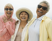 Three older women laughing together on a beach