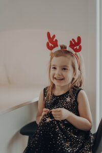 Young child living with autism smiling while wearing red reindeer antlers 