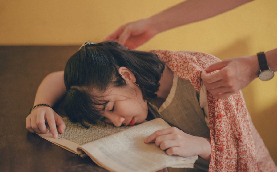 Someone covers a young woman who fell asleep reading with a blanket