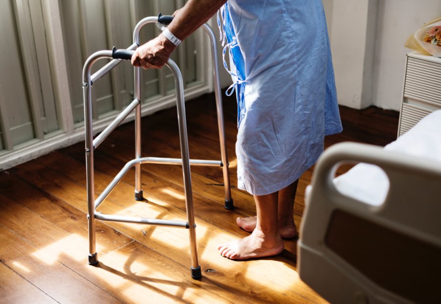 A person wearing a hospital gown walks using a walker