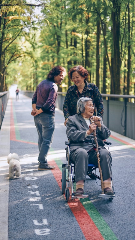 A woman pushes her mom in a wheelchair down a walking path