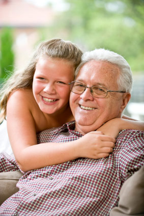 A grandpa smiling while his granddaughter hugs him from behind