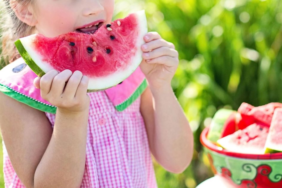 Little girl in a striped pink dress eating a slice of watermelon