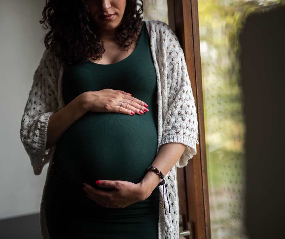 Pregnant woman holding belly, dressed in dark green